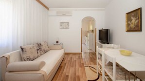 A modern living room with a sofa, a dining table, a TV, and a painting on the wall.