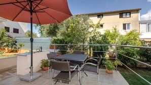 An outdoor patio with a table and chairs, surrounded by potted plants and a red umbrella.