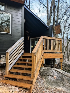 Une cabane avec un escalier en bois menant à une terrasse, le tout entouré d’arbres.
