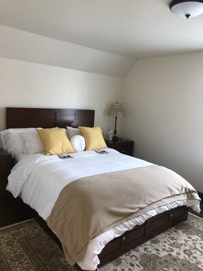 Cama bem arrumada com cabeceira de madeira escura, roupa de cama branca e dois travesseiros amarelos.