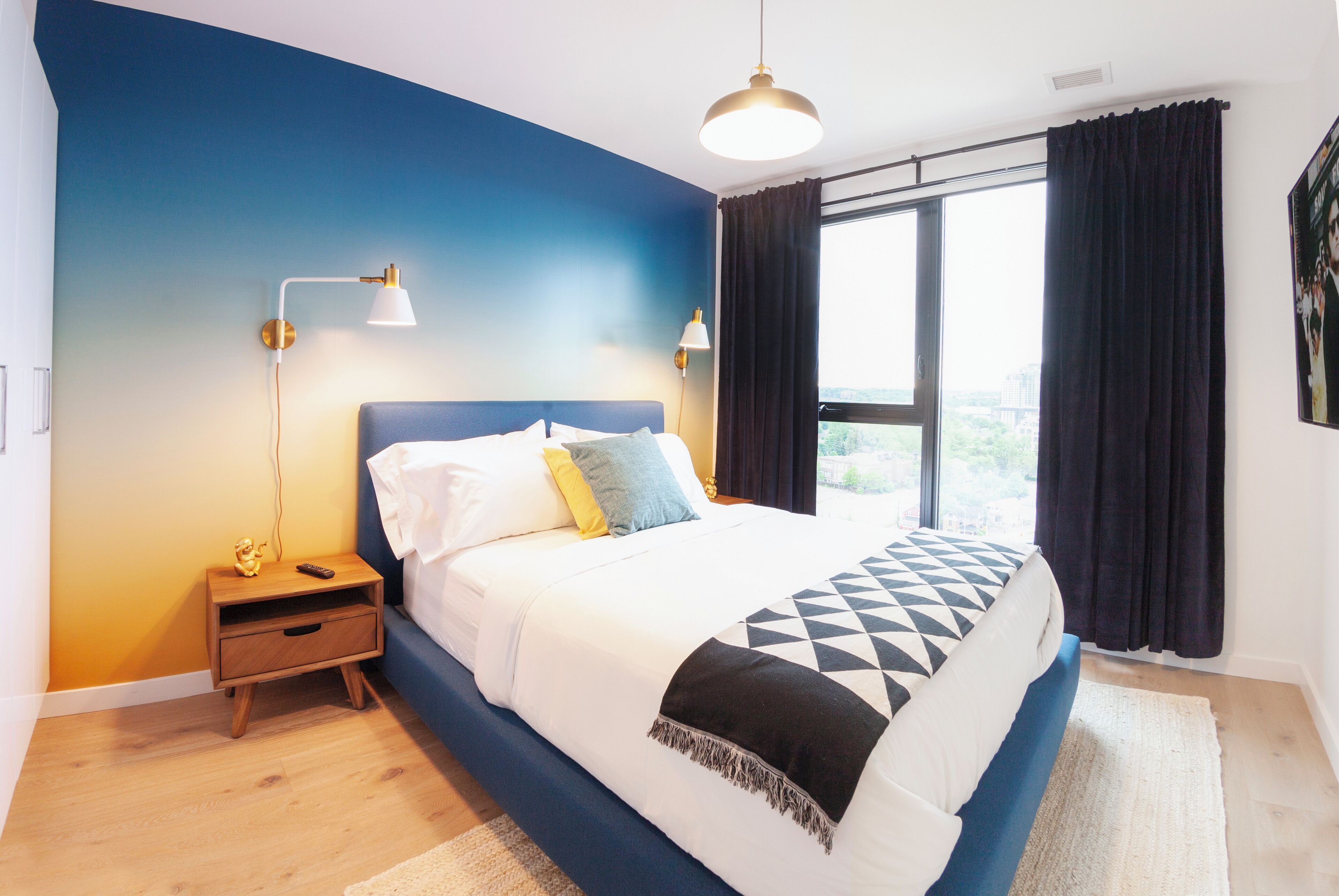 A bedroom with a bed, nightstands, a window with curtains, and a view of the outdoors.