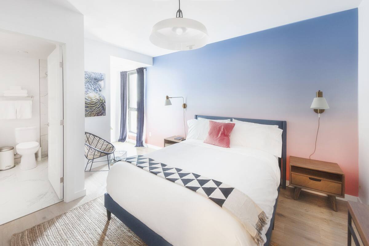 A modern bedroom with a bed, bedside tables, a chair, and a view of the bathroom.