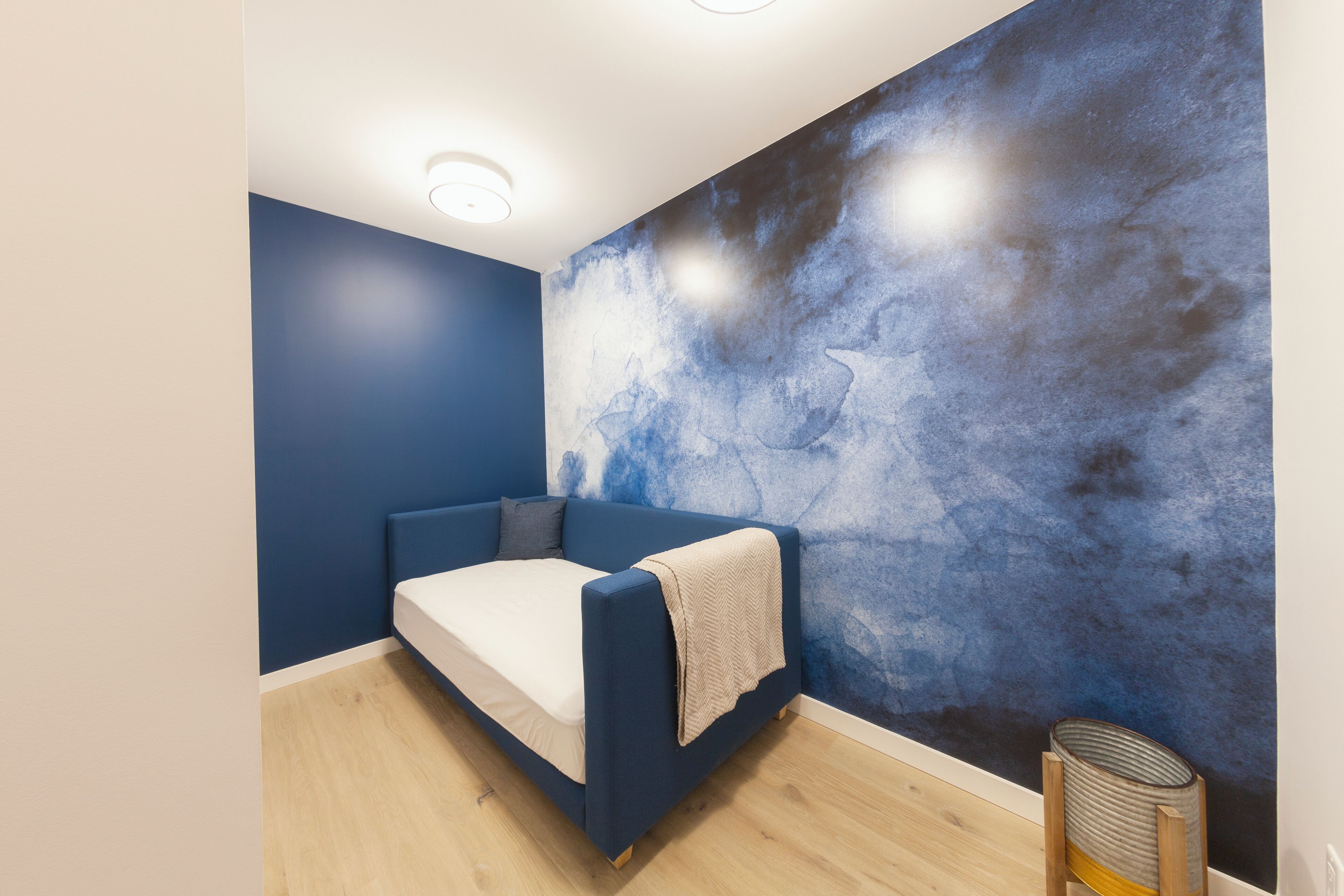 A room with a blue sofa, a white mattress, a textured blue wall, and a small table with a basket.