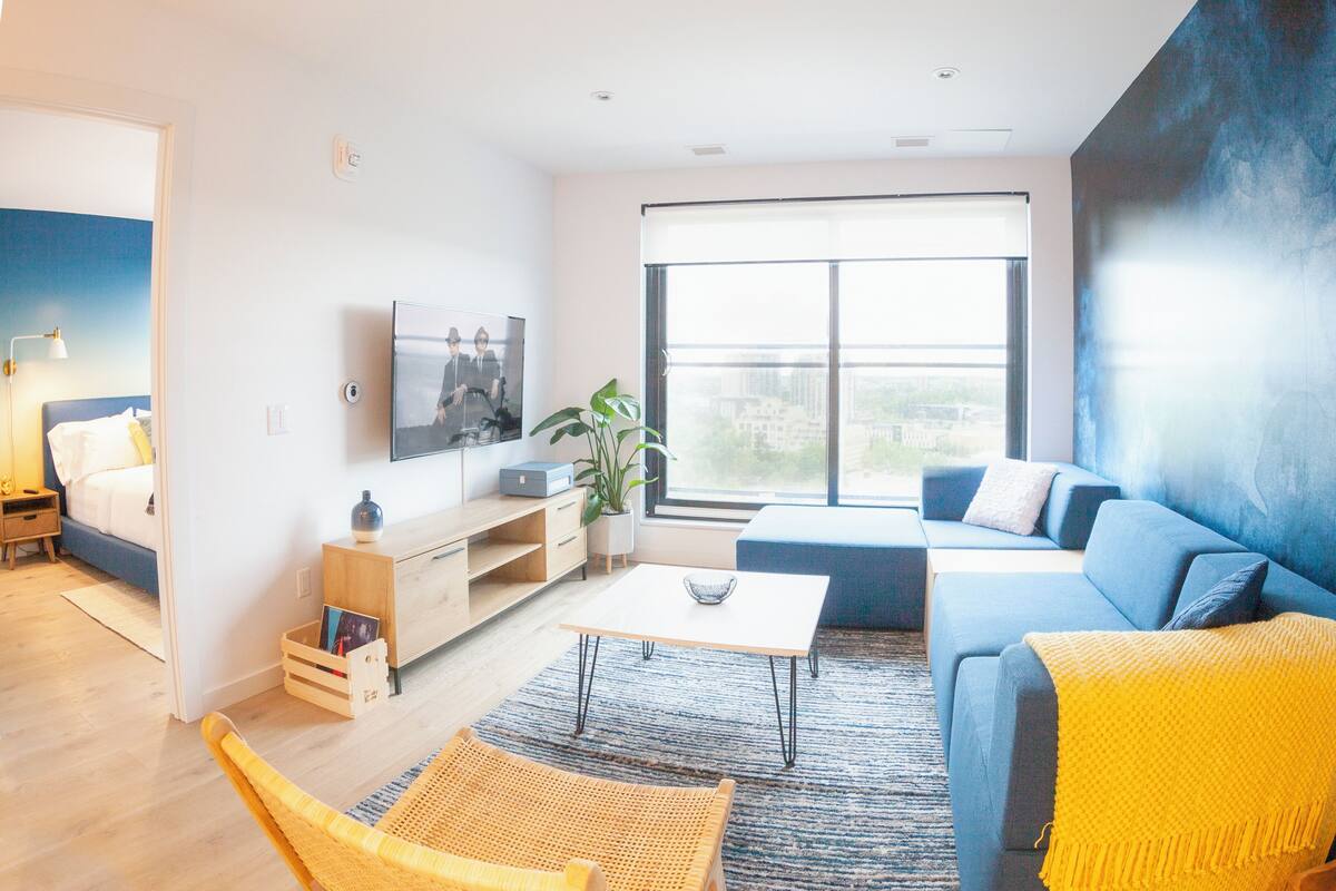 A modern living room with a sofa, a coffee table, a TV, and a large window with a city view.