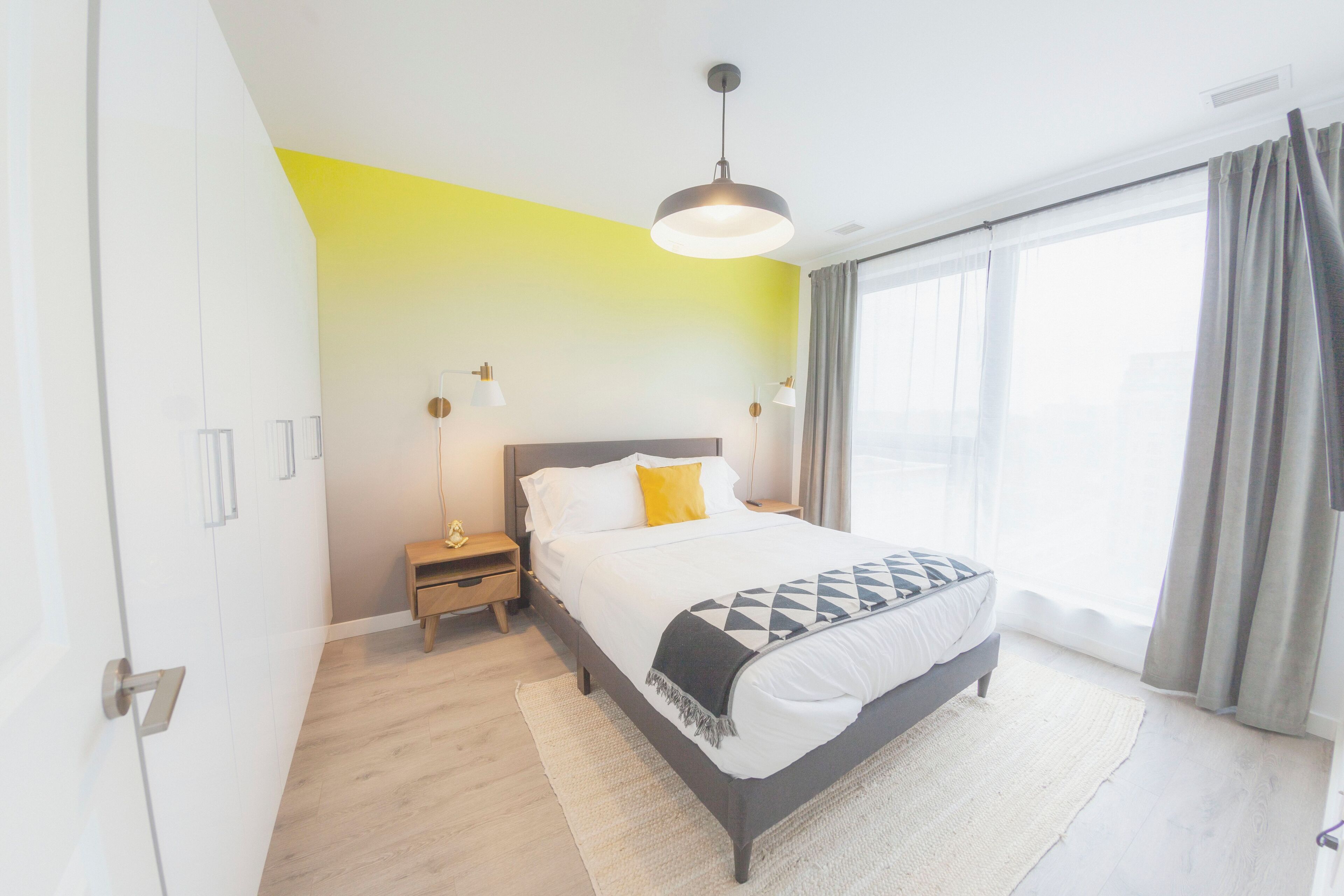 A modern bedroom with a bed, bedside tables, and a large window with curtains.