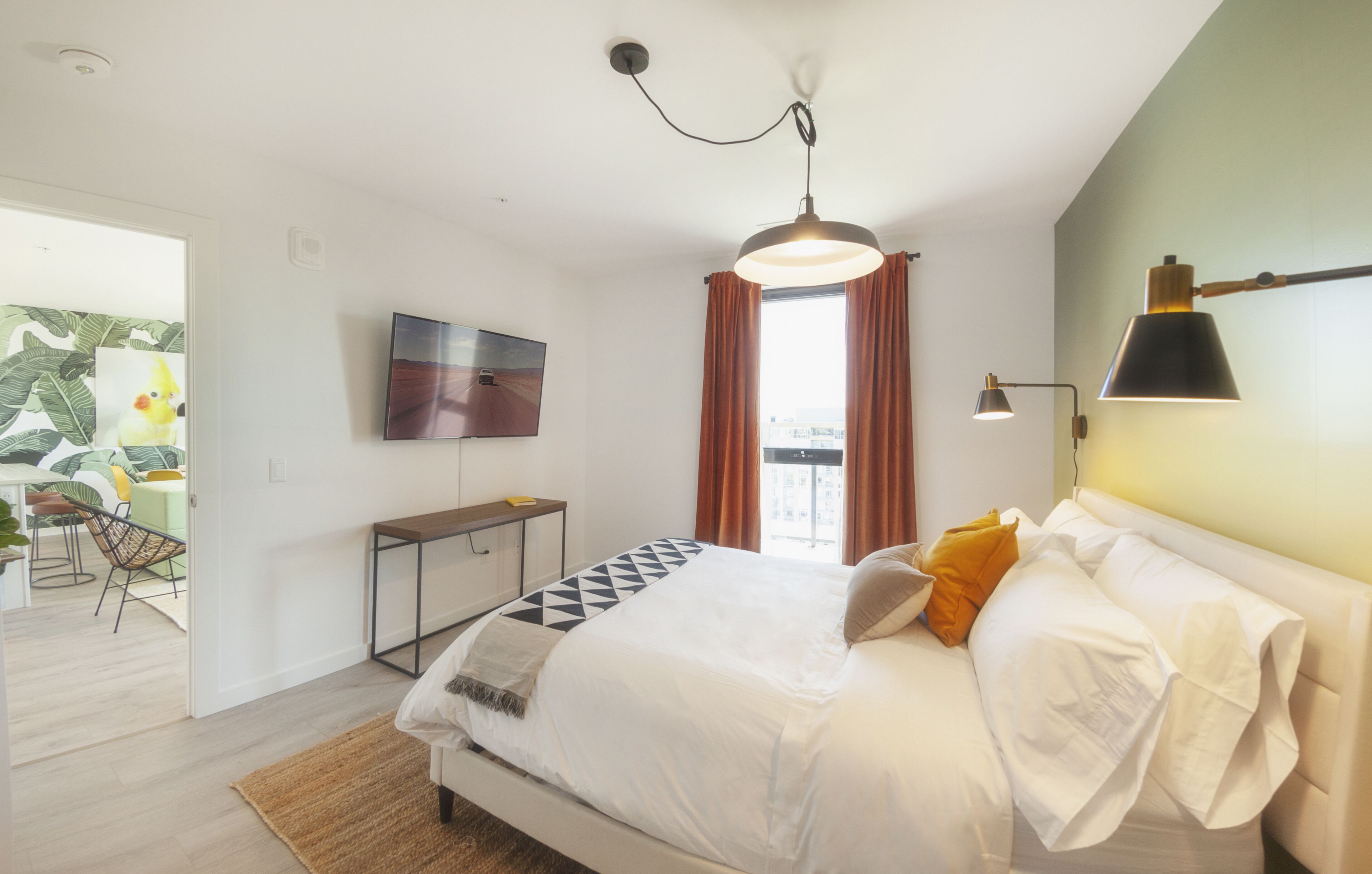 Un dormitorio moderno con cama, escritorio, televisor y ventana con cortinas.