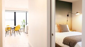 Ein modernes Hotelzimmer mit Bett, Nachttischlampe und Blick auf die Stadt durch große Fenster.