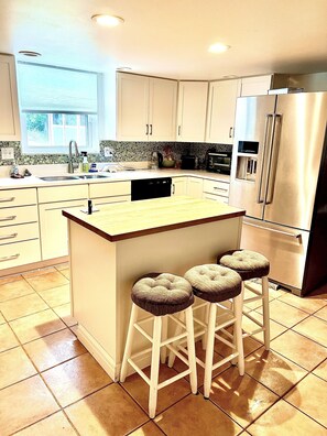 A modern kitchen with a central island, bar stools, stainless steel appliances, and a window providing natural light. - The Art of Seclusion (Yellow Springs)