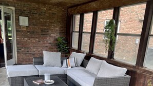 Ein überdachter Patio-Bereich mit einer Eckcouch, einem kleinen Tisch und einem Blumentopf.