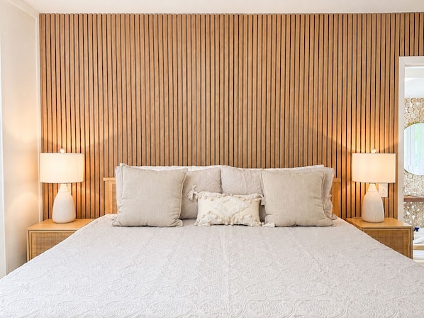 A bedroom with a wooden slat headboard, a large bed with multiple pillows, and two bedside lamps.