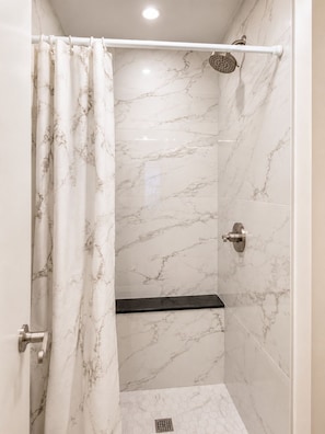 Une douche avec un mur en marbre, un pommeau de douche et un rideau.