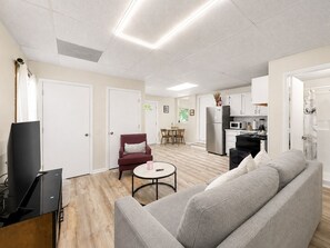 Een moderne woonkamer met een grijze bank, een klein rond tafeltje en een flatscreen televisie.