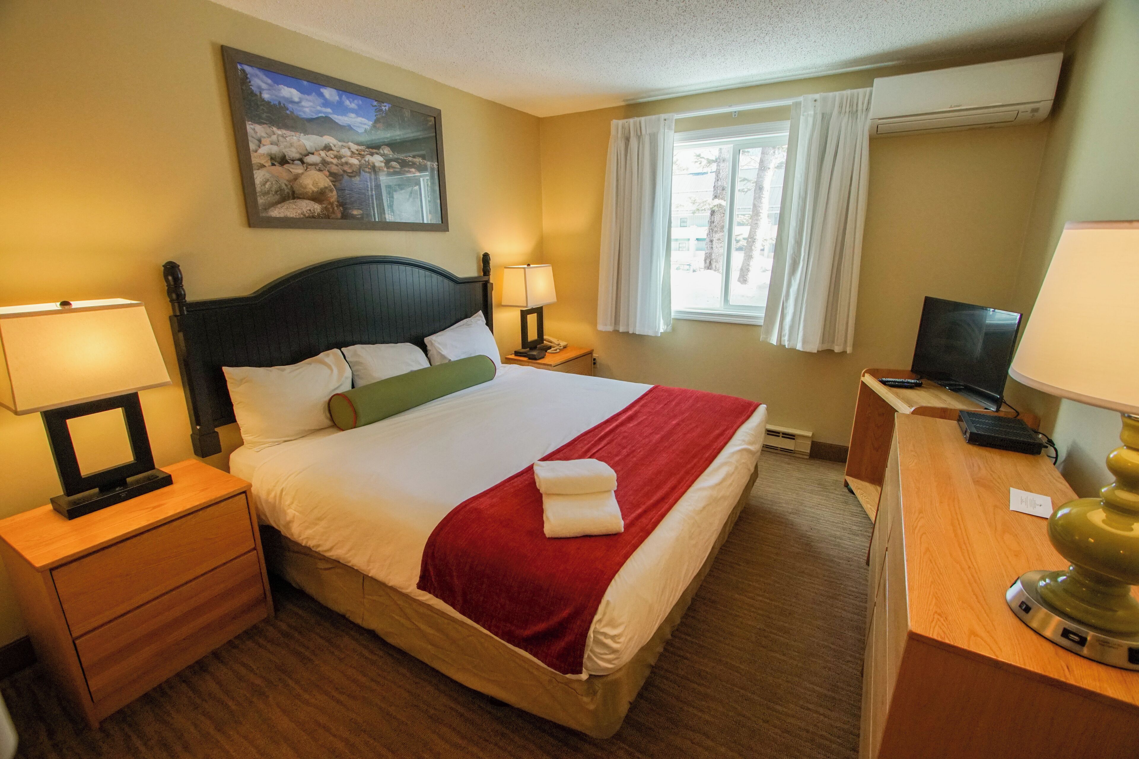 A hotel room with a bed, nightstands, a desk, a television, and a window with curtains.