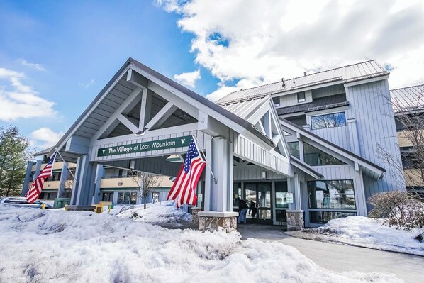 A building with a sign reading "The Village of Loon Mountain" and two American flags. - The Village of Loon Mountain Fixed Rooms (Lincoln)