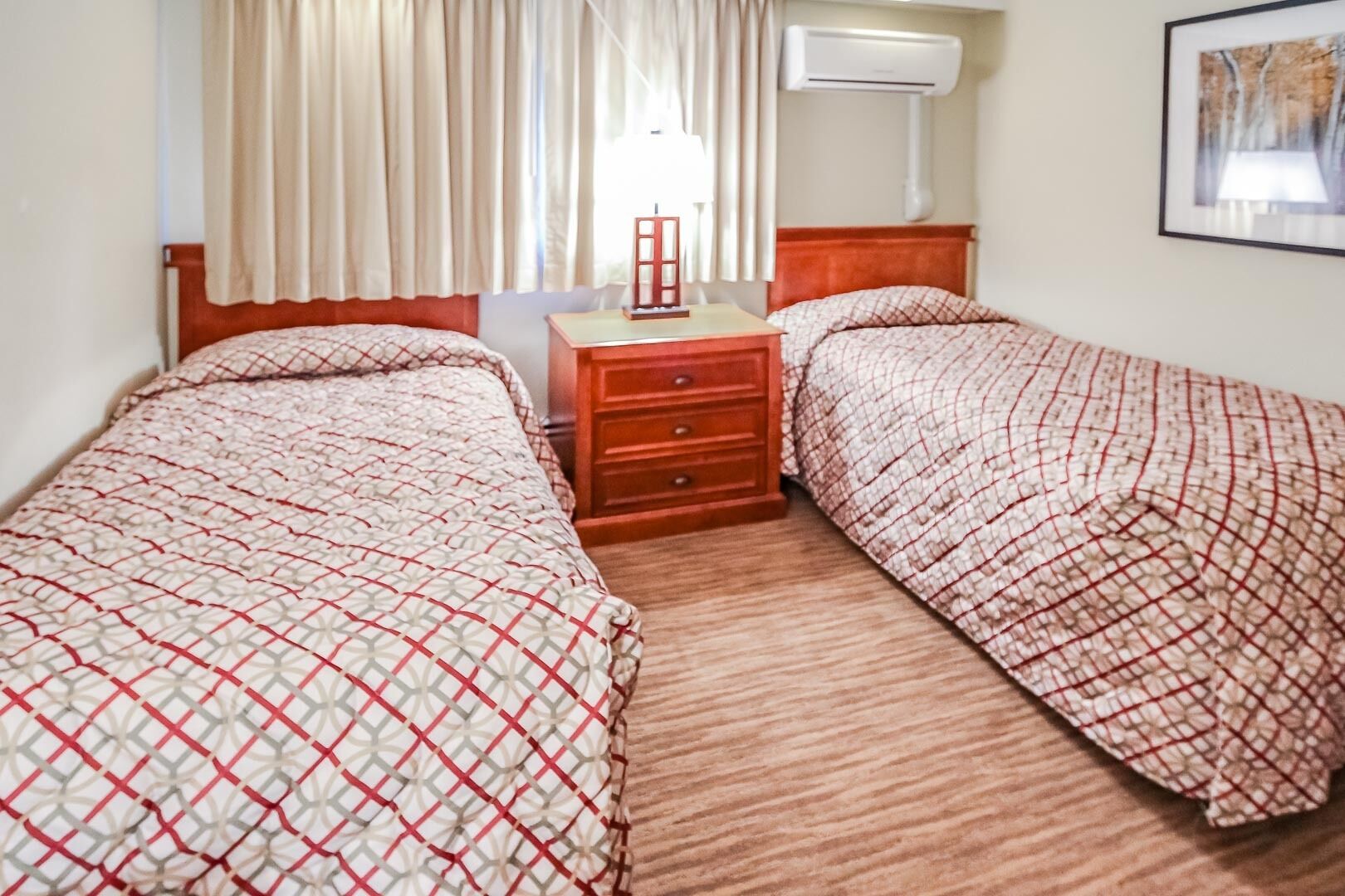 A hotel room with two beds, a nightstand, a lamp, and an air conditioning unit.