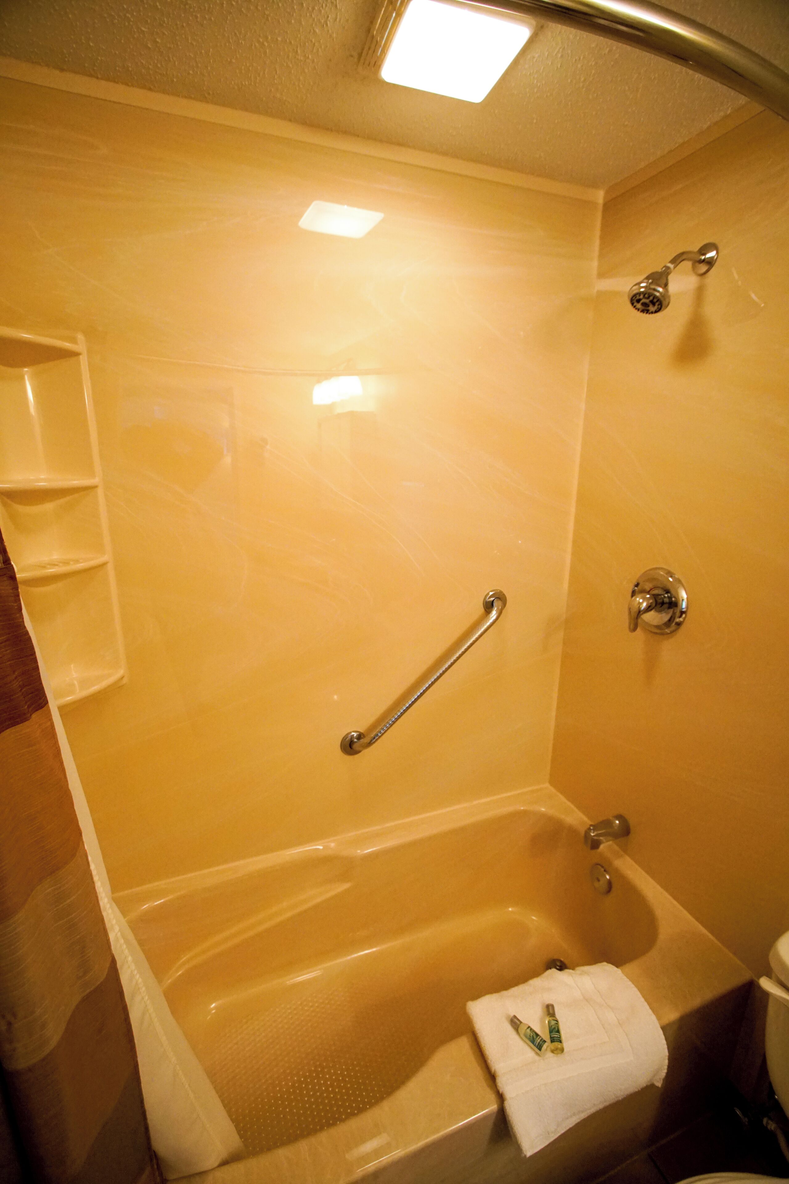 Une salle de bain équipée d’une baignoire, d’une douche et de toilettes. Il y a une barre d’appui dans la douche et un porte-serviettes sur lequel est accrochée une serviette.