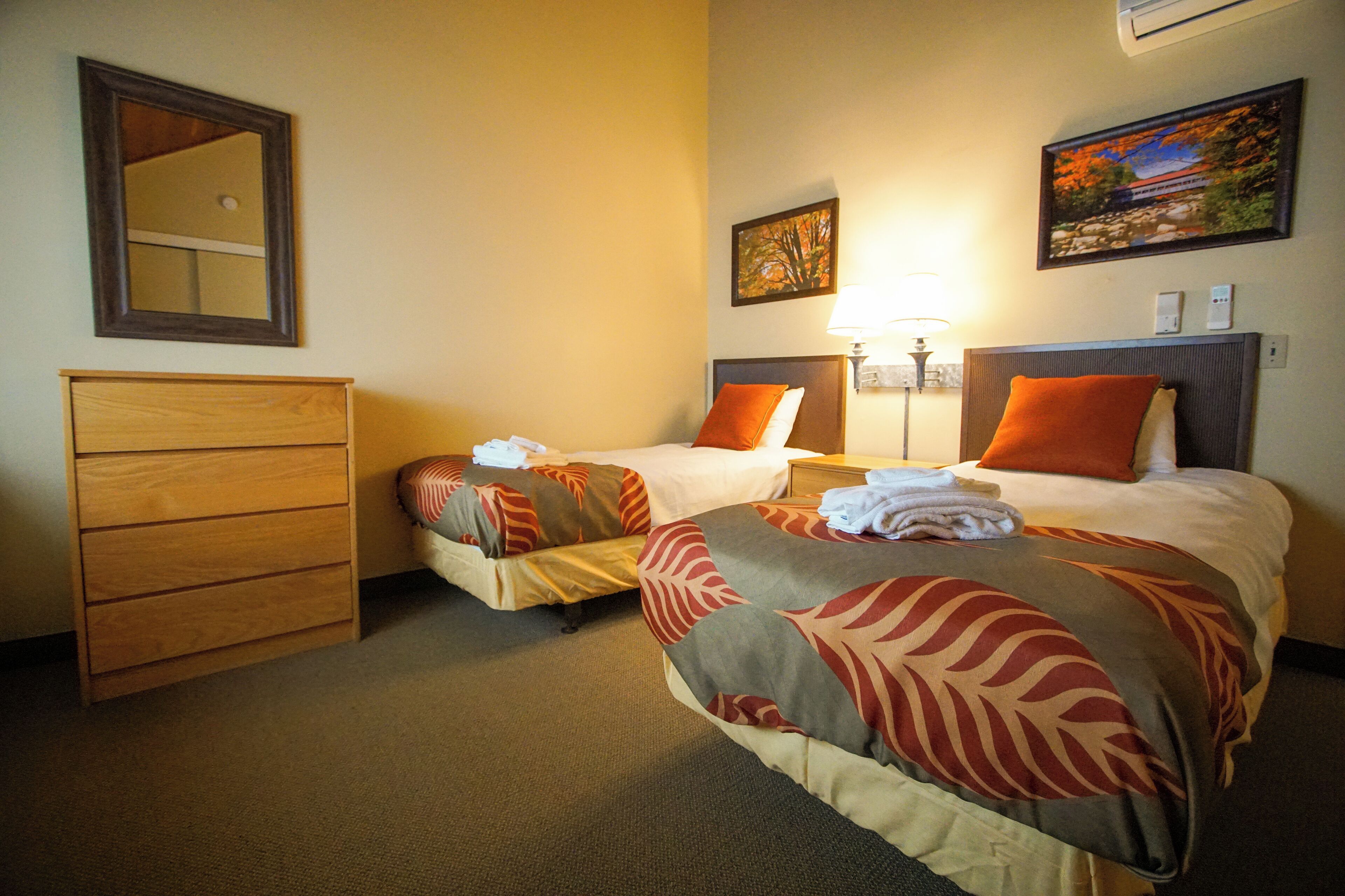A hotel room with two beds, a wooden dresser, a mirror, and a painting on the wall.