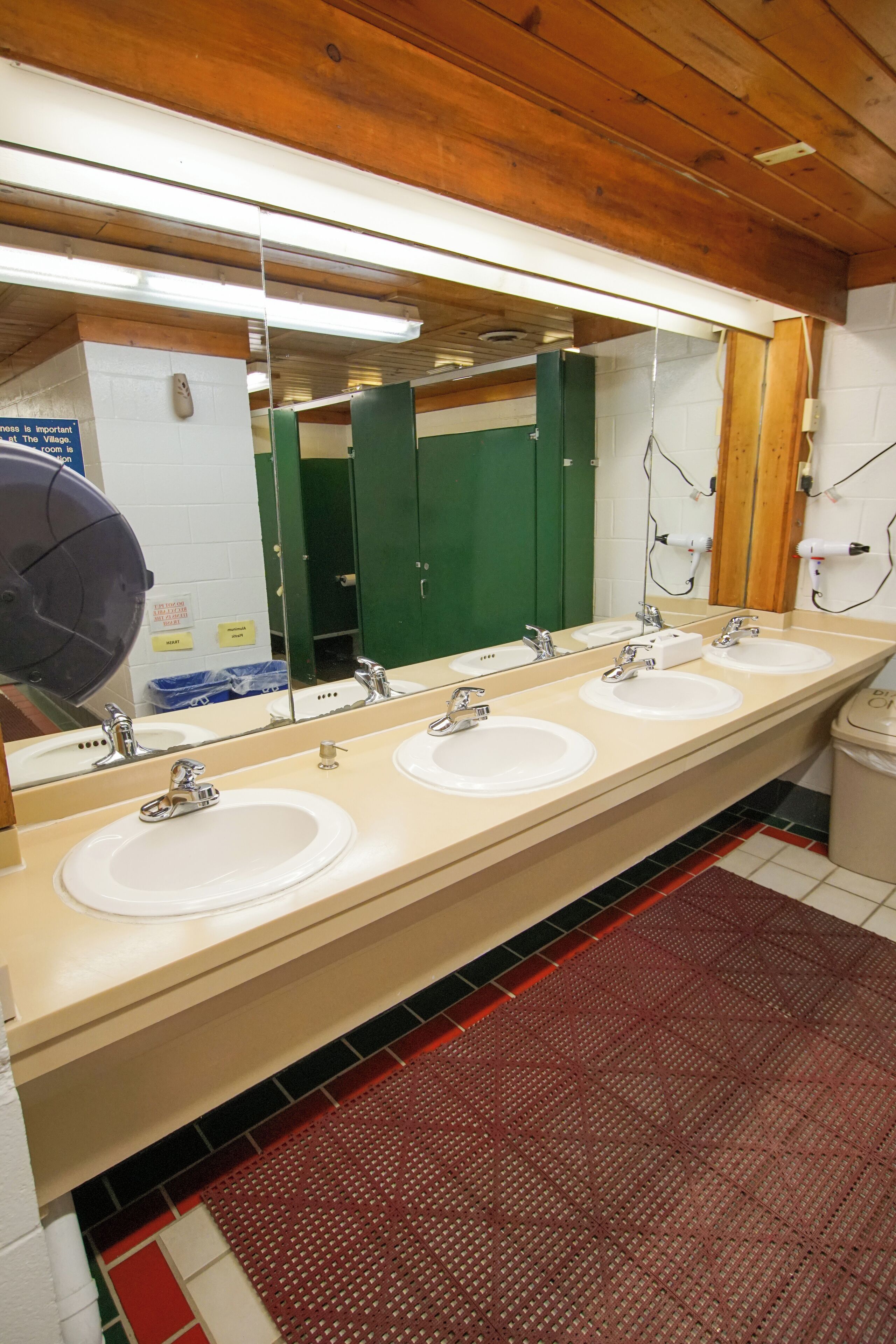 A public restroom with three sinks, a large mirror, and a red patterned mat on the floor.