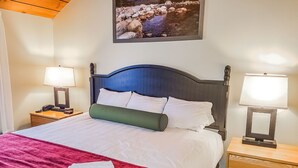 Hotellihuoneessa on sänky, kaksi yöpöytää, joissa on lamput, punainen heittopeitto ja seinällä oleva kehystetty kuva joesta.