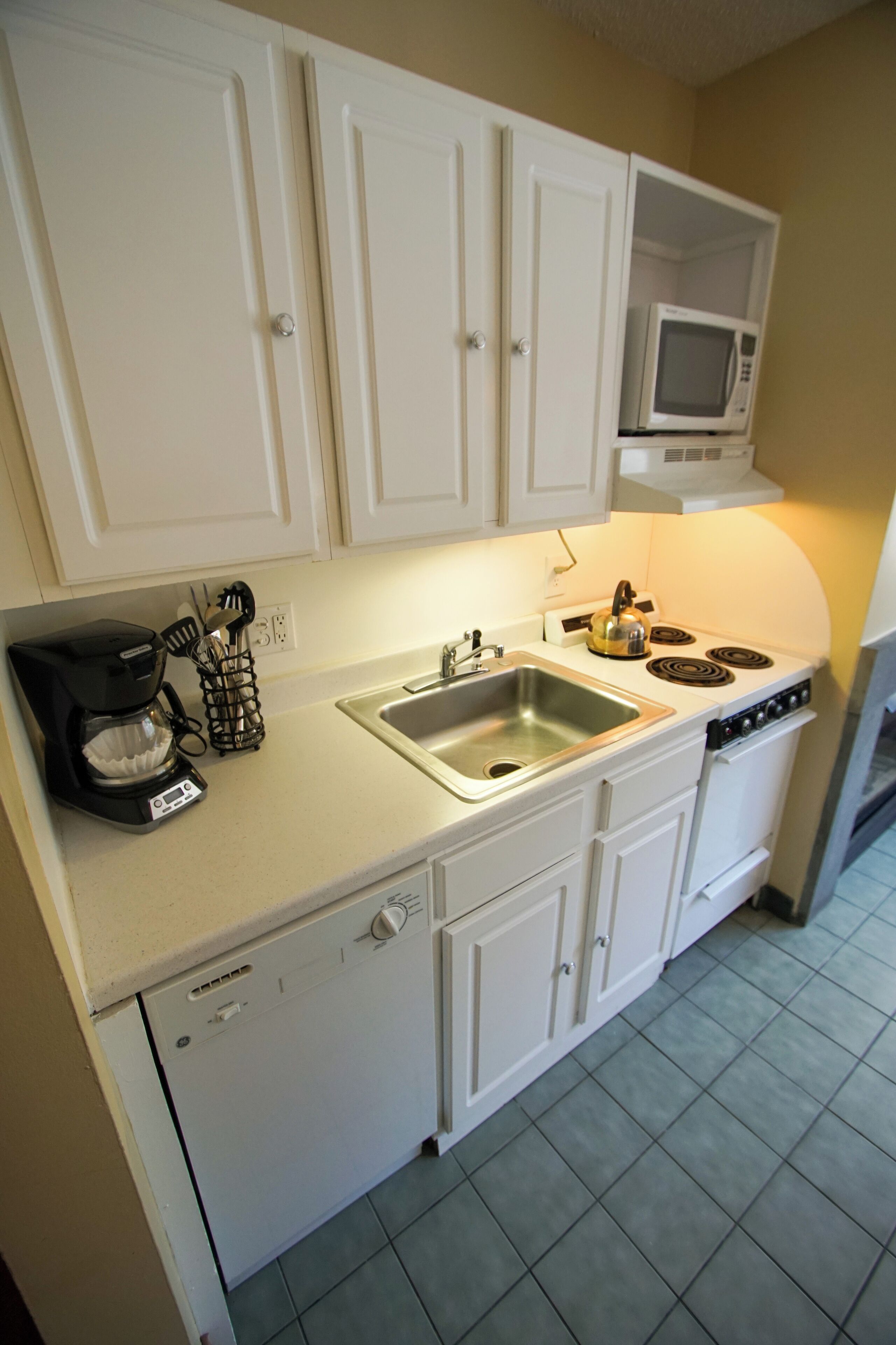 A compact kitchen with white cabinets, a built-in microwave, a coffee maker, and a dishwasher.
