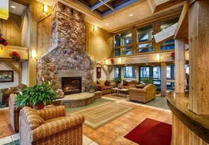 A spacious lobby with a stone fireplace, wooden walls, and large windows. - The Village of Loon Mountain Fixed Rooms (Lincoln)
