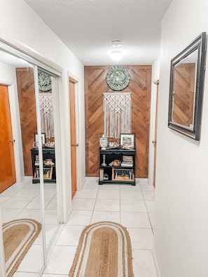 Symmetrical hallway with a decorative macramé piece and mirror, featuring a tiled floor and two rugs.