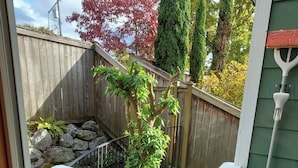 A view of a wooden deck with a white railing, a stone wall, and a green building in the background. - Judkins Park Light Rail Townhouse Haven (Seattle)