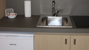 Een keuken met een roestvrijstalen spoelbak, houten kastjes en planken met witte borden en bekers.