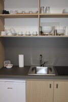 Una cocina con un lavamanos de acero inoxidable, armarios de madera y estantes con vajilla y tazas blancas.