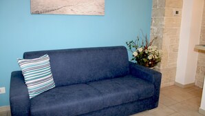 Een donkerblauwe bank met een gestreept kussen tegen een lichtblauwe muur, een accentmuur van steen en een bloemstuk.