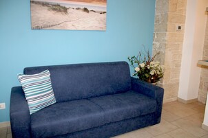 A dark blue sofa with a striped pillow against a light blue wall, a stone accent wall, and a floral arrangement.