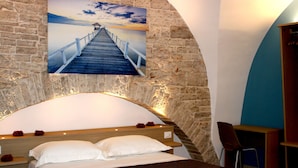 Een slaapkamer met een stenen muur, een houten hoofdbord, een bed met witte lakens en een schilderij van een pier.