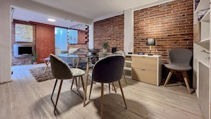 A modern living room with a brick wall, a glass dining table, and wooden chairs. - Mi Zona Lodging Coyoacán B (Mexico City)