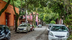 A cobblestone street lined with parked cars and buildings, including a pink building with a red roof. - Mi Zona Lodging Coyoacán B (Mexico City)