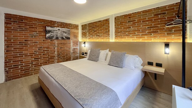 A hotel room with a large bed, a brick wall, and a picture of a building. - Mi Zona Lodging Coyoacán B (Mexico City)