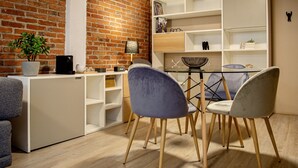 A compact living space with a brick wall, a white shelving unit, and a dining area with two chairs and a glass table. - Mi Zona Lodging Coyoacán B (Mexico City)
