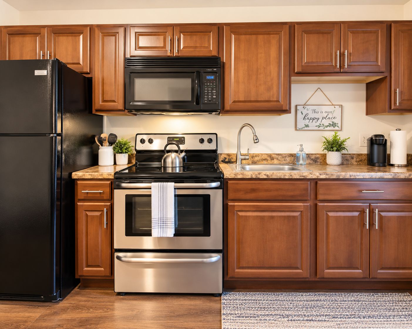 A kitchen with a black refrigerator, stainless steel oven, and a microwave. There is a granite countertop, wooden cabinets, and a stainless steel sink.