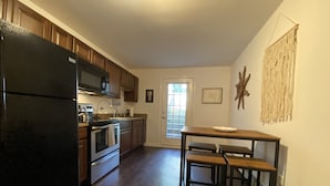 A kitchen with wooden cabinets, a black refrigerator, stainless steel appliances, and a dining table with benches. - Comfy, private one Bedroom Apartment with full kitchen, living room, full bath. (Ridge)