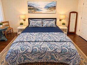 A bedroom with a large bed, two bedside tables, a chair, a painting on the wall, and a door. - Private One Bedroom Apartment with full kitchen, LR, full bath and private yard (Ridge)