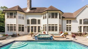 Une grande maison avec une piscine, de nombreuses fenêtres et du mobilier d’extérieur.