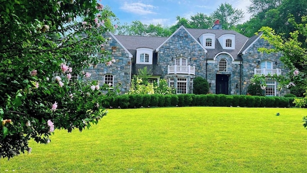 Une grande maison en pierre, dotée d’une pelouse bien entretenue et agrémentée de fleurs en pleine floraison.
