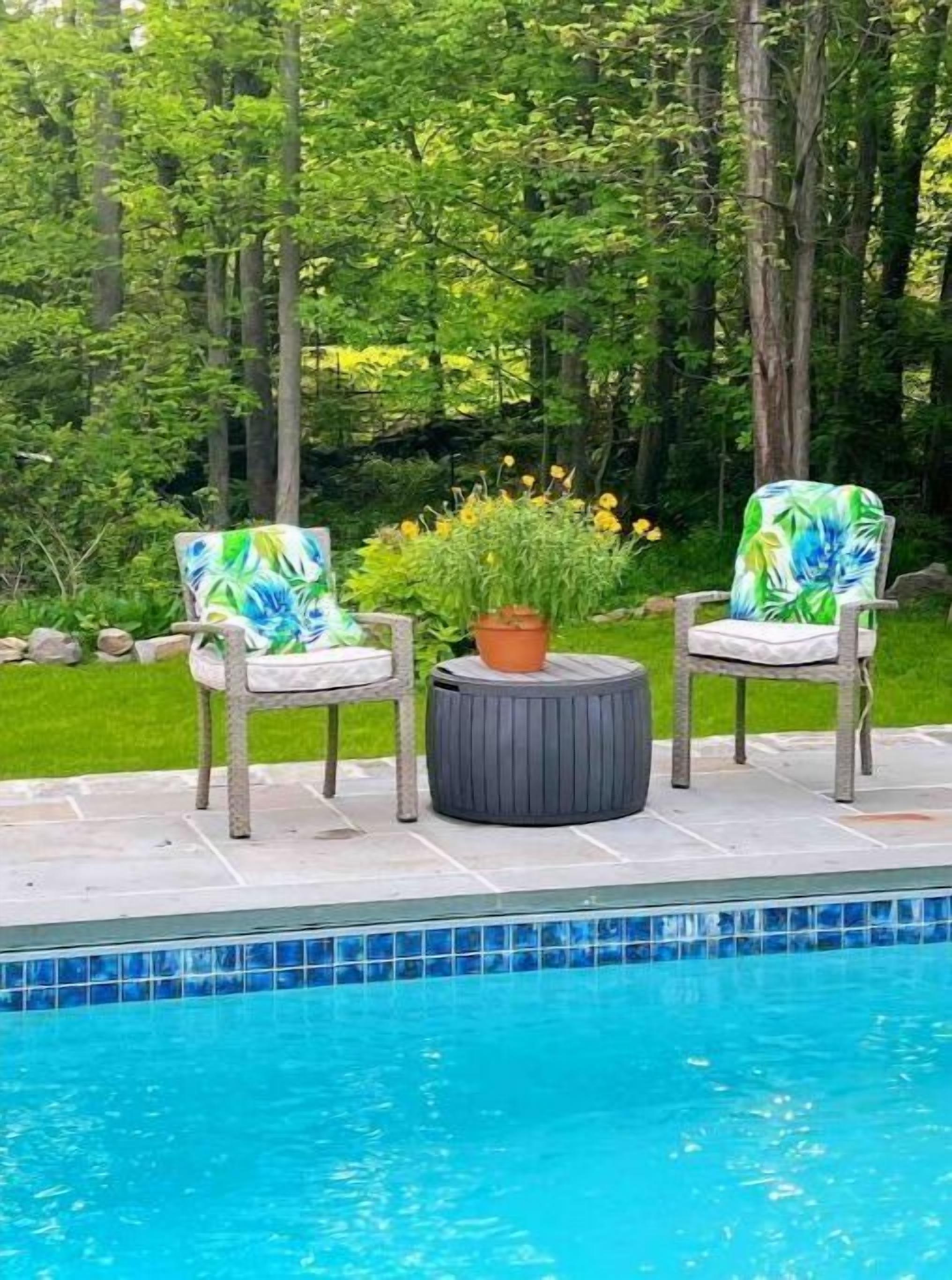 Un espace aménagé au bord de la piscine, comprenant deux chaises, une table ronde et un pot de fleurs.