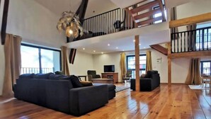 A spacious living area with a large black sofa, wooden flooring, a ceiling light fixture, and a balcony with a railing. - Large, charming family home in the beautiful Auvergne village of Blesle (Blesle)
