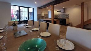 A dining area with a large table set for six, a kitchen in the background, and a view through a large window. - Large, charming family home in the beautiful Auvergne village of Blesle (Blesle)