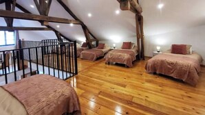 A spacious attic bedroom with wooden beams, four beds, and a black railing. - Large, charming family home in the beautiful Auvergne village of Blesle (Blesle)