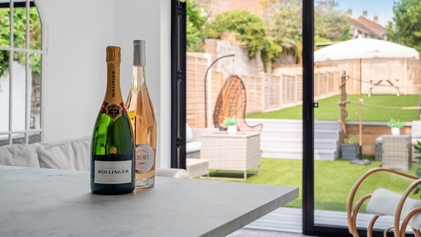 A room with a view of a garden through a glass door, featuring two bottles of champagne on a table. - Bay View Luxury Stays - Iris Boutique Harbour Cottage, walking distance to Beach (Weymouth)