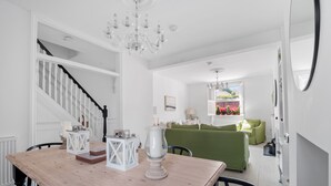 A dining area with a wooden table, white lanterns, and a chandelier. A staircase with white railings leads to an upper floor. A green sofa is visible in the background. - Bay View Luxury Stays - Iris Boutique Harbour Cottage, walking distance to Beach (Weymouth)