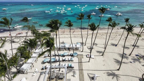 A beach resort with a pool area, palm trees, and boats in the water. - Best View Beach front Apartment In Punta Cana (Punta Cana)