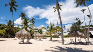 A beach with thatched umbrellas, palm trees, and sun loungers. - Luxury 3BR beachfront Condo in Punta Cana (Punta Cana)