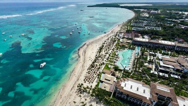 An aerial view of a coastal resort with a beach, clear waters, and a hotel with multiple buildings. - Luxury 3BR beachfront Condo in Punta Cana (Punta Cana)